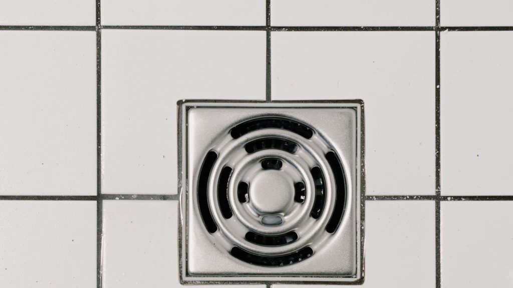 Chrome shower drain cover in a tiled shower floor before cleaning
