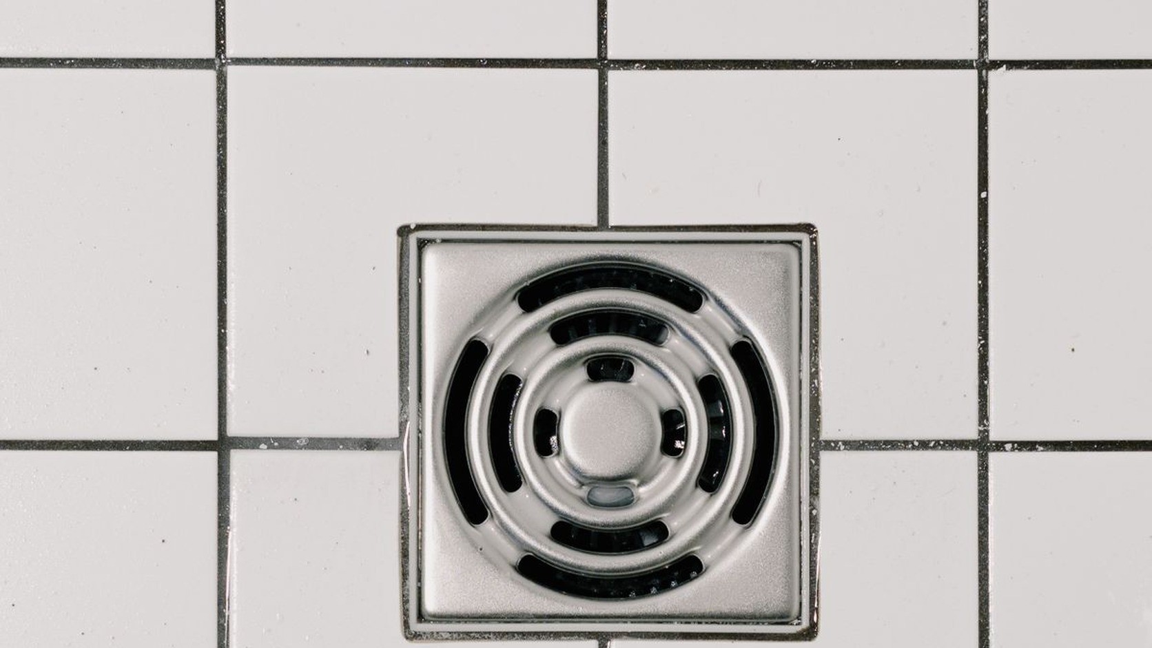 Chrome shower drain cover in a tiled shower floor before cleaning